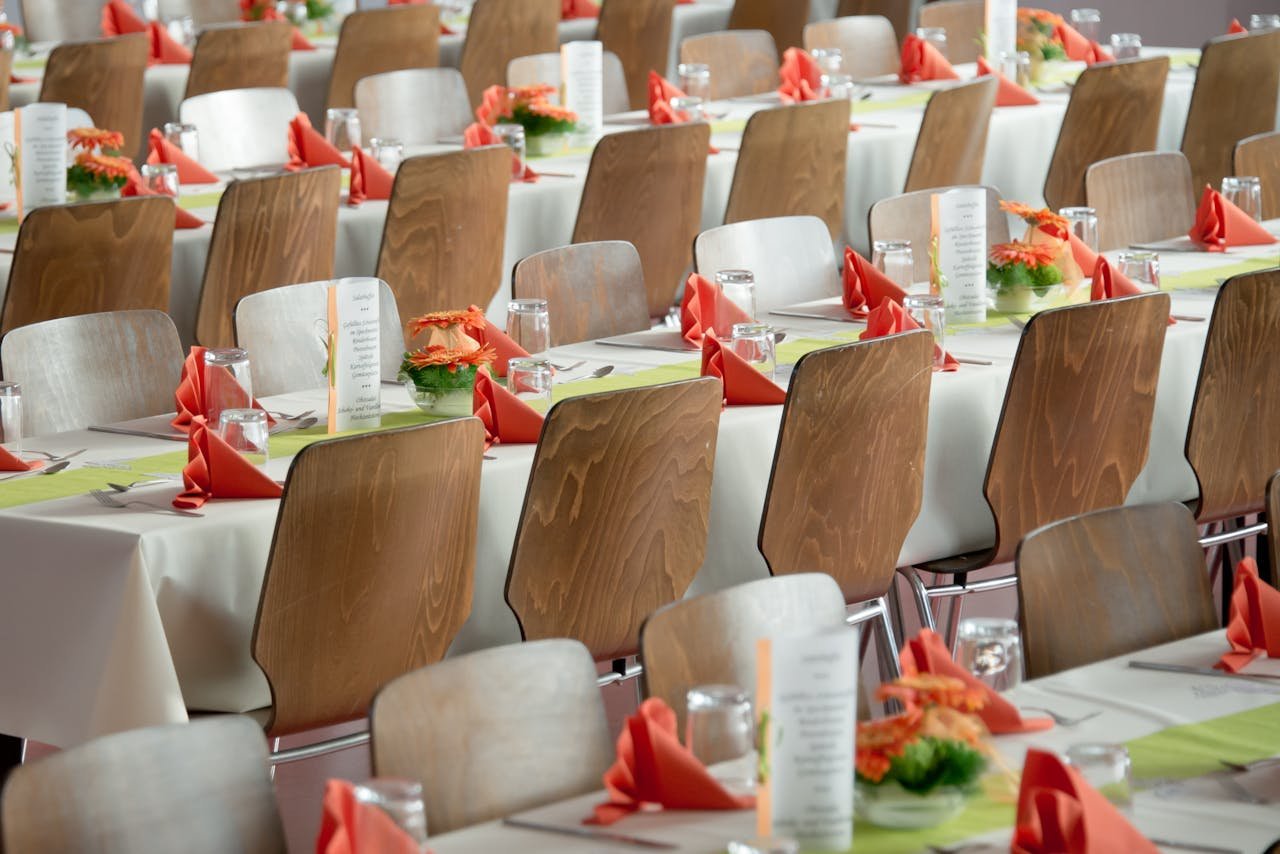 about-01 Beautifully arranged tables with wooden chairs for a formal event, adorned with orange flowers.